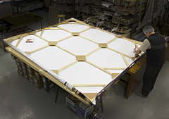 A large, square gallery wrapped canvas being mounted on a stretcher bar frame
